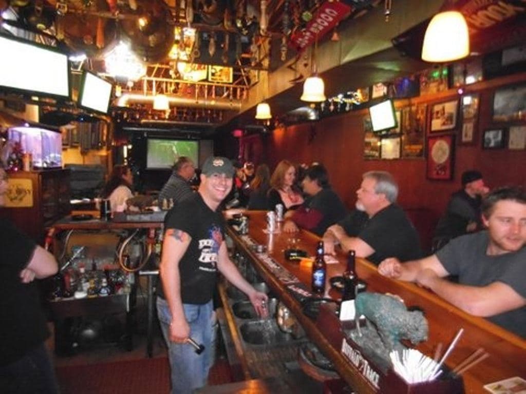 Drinkers along both sides of the bar rail with bottles in front of them, a bartender coming down the duckboards, memorabilia and televisions on every wall.